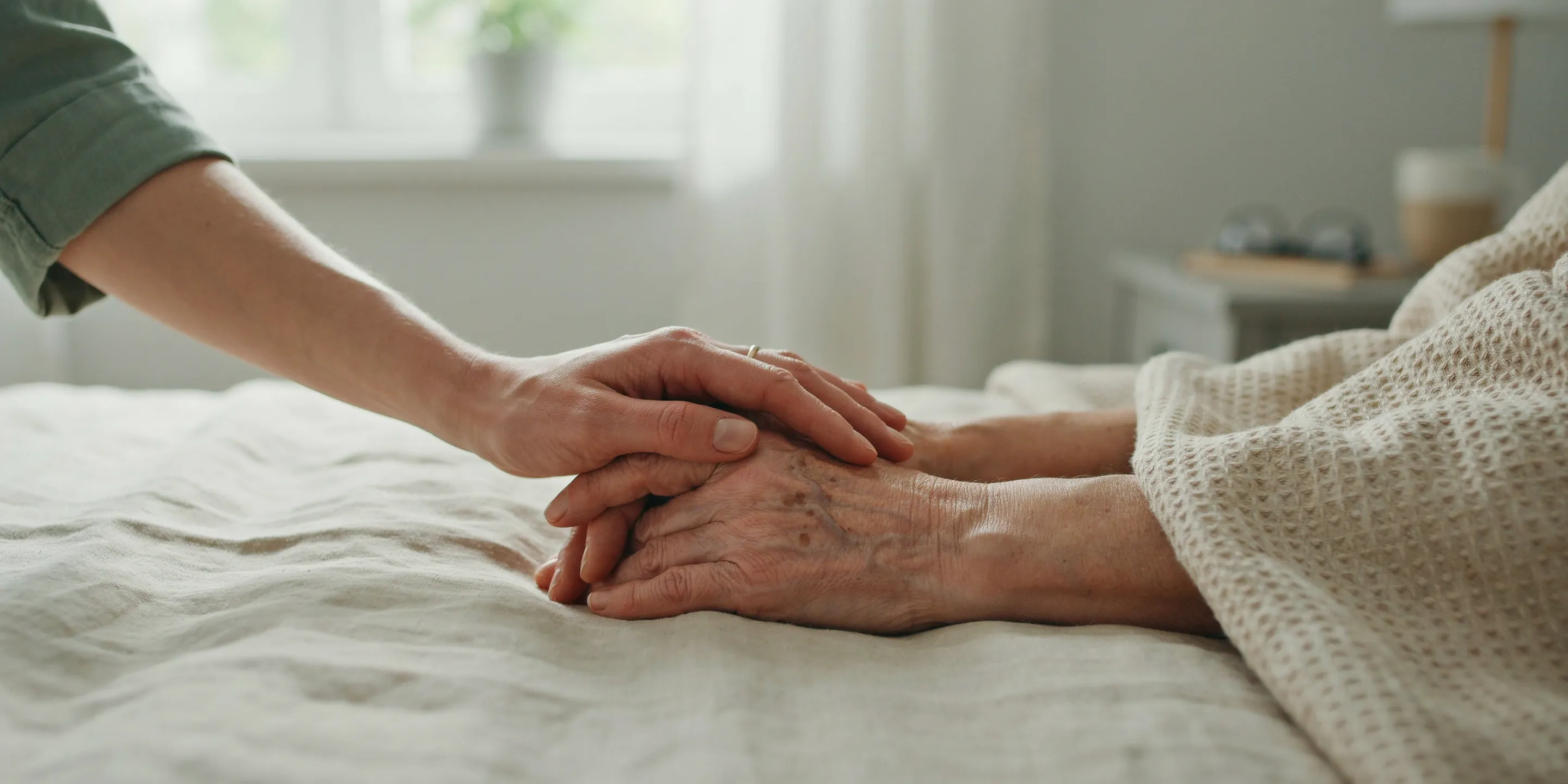 A family member holding an elder's hands in a peaceful, sunlit room